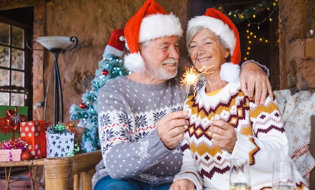 Feliz casal sênior em chapéus de Papai Noel sorrindo e abraçando em casa na época do Natal com estrelinhas Conceito de amor familiar de Natal