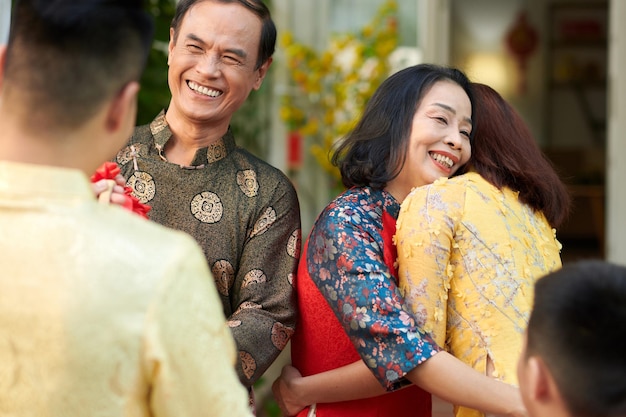 Feliz casal sênior em vestidos tradicionais ao dai cumprimentando e abraçando seus filhos adultos que vieram...