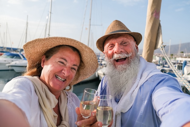 Feliz casal sênior fazendo selfie, torcendo com champanhe em um veleiro durante as férias de aniversário