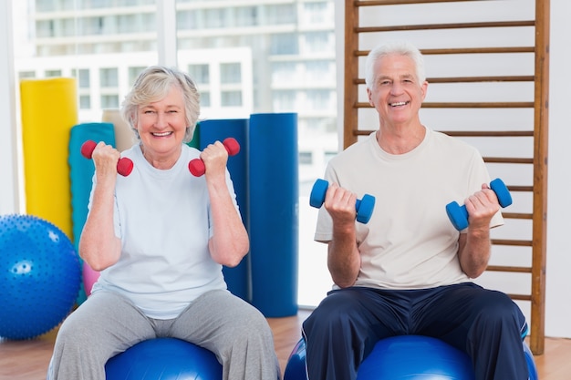 Feliz casal sênior levantando dumbbells na bola de exercício