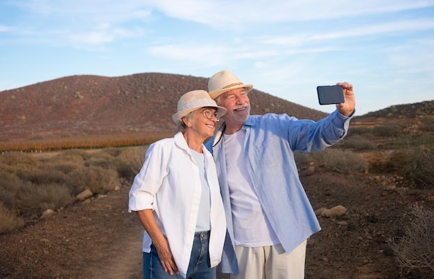 Feliz casal sênior maduro e ativo desfrutando de excursão ao ar livre à luz do pôr do sol tirando uma selfie