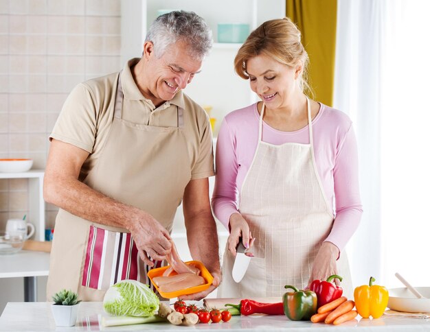 Feliz casal sênior preparando comida na cozinha.