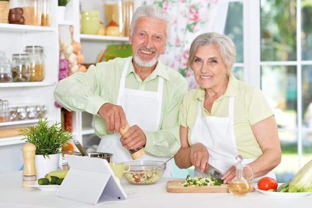 Feliz casal sênior preparando o jantar junto com o tablet na mesa