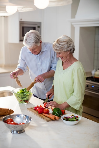 Feliz casal sênior preparando salada de legumes