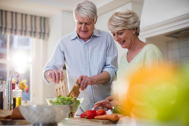 Feliz casal sênior preparando salada de legumes