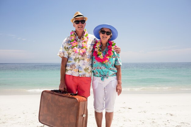 Feliz casal sênior segurando a mala na praia