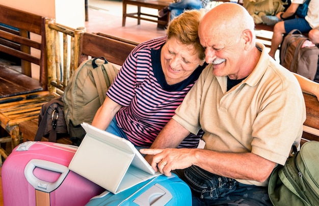 Foto feliz casal sênior sentado com laptop digital e bagagem de viagem durante a aventura ao redor do mundo