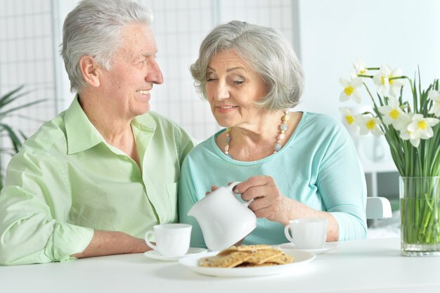 Feliz casal sênior sentado na mesa da cozinha e bebendo chá