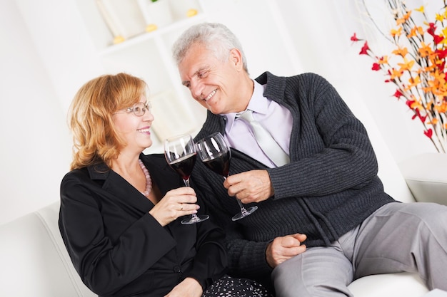 Feliz casal sênior sentados juntos em casa, sorrindo e bebendo vinho tinto.