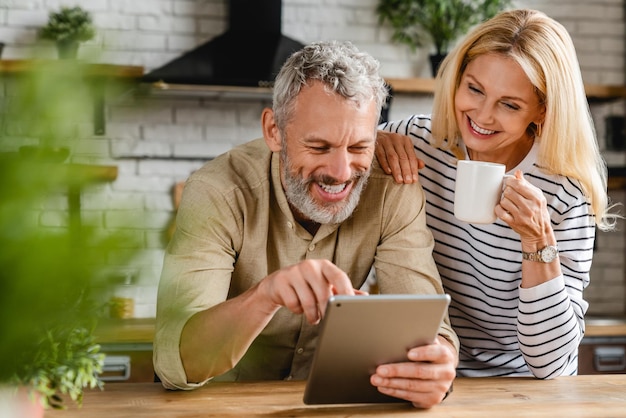 Feliz casal sênior usando tablet digital na cozinha em casa