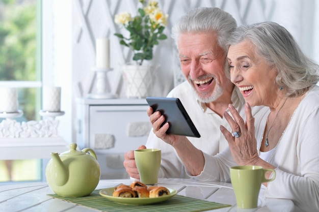 Feliz casal sênior usando tablet enquanto bebe chá na cozinha