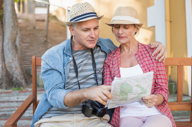 Feliz casal turista olhando o mapa em um banco na cidade