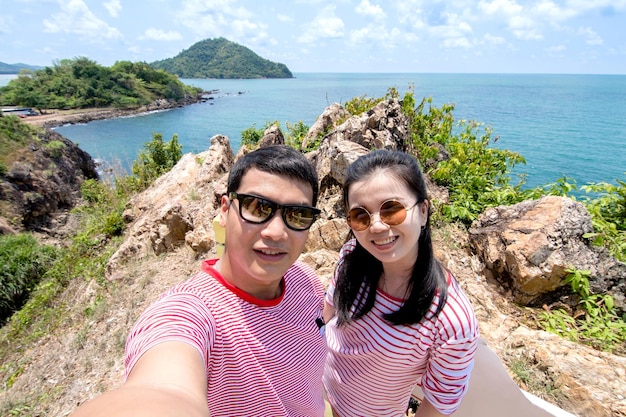 Feliz casal viajando tomando selfie na montanha contra o oceano