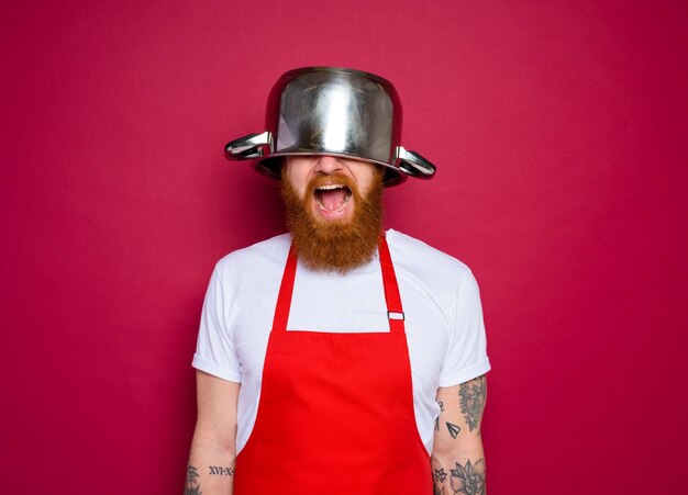 Foto feliz chef con barba y delantal rojo juega con olla