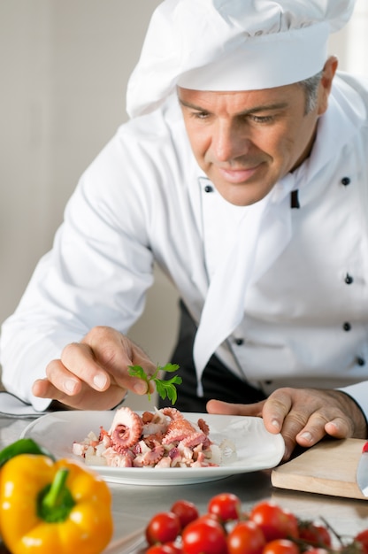 Feliz chef maduro adornar una ensalada de calamar con persil en la cocina del restaurante