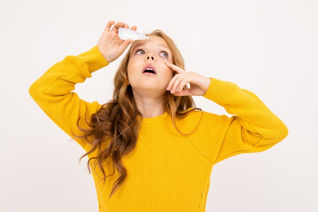 Feliz chica adolescente con el pelo rojo, con capucha y pantalones amarillos tiene lentes de contacto aisladas sobre fondo blanco.