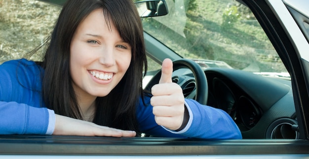 Feliz chica adolescente con un pulgar arriba sentado en su coche