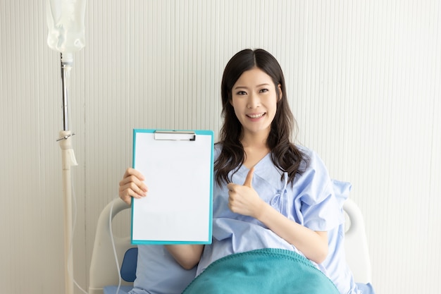 Feliz chica asiática en una cama de hospital con un papel en blanco