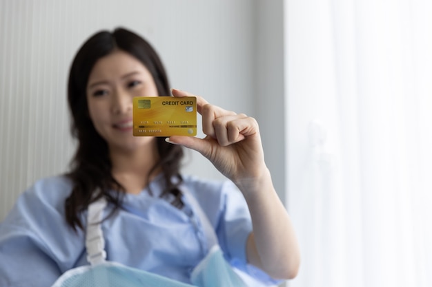 Feliz chica asiática en una cama de hospital con tarjeta de crédito