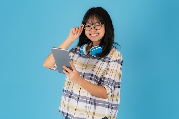 Feliz chica asiática de pie con el uso de la tableta sobre un fondo azul.