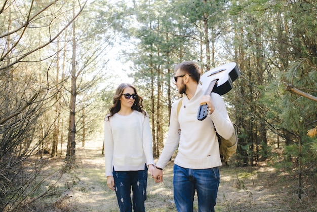 Feliz chica y chico con mochila turística y guitarra caminando en la naturaleza, concepto de historia de amor de viaje, enfoque selectivo