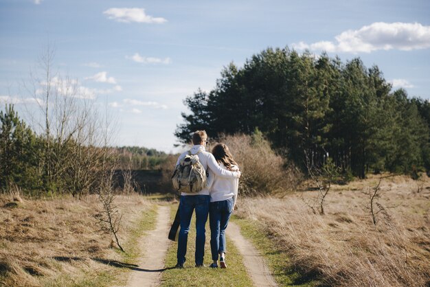 Feliz chica y chico con mochila turística y guitarra caminando en la naturaleza, concepto de historia de amor de viaje, enfoque selectivo