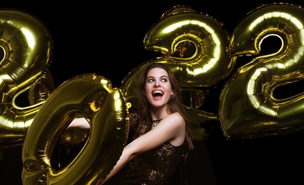 Feliz chica hermosa en elegante vestido de fiesta sexy con globos de oro 2022, divirtiéndose en Navidad o fiesta de fin de año.