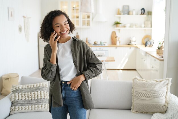 Feliz chica hispana habla por teléfono inteligente en casa y se ríe Discusión distante