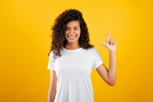 Feliz chica negra mostrando dos dedos aislados sobre amarillo