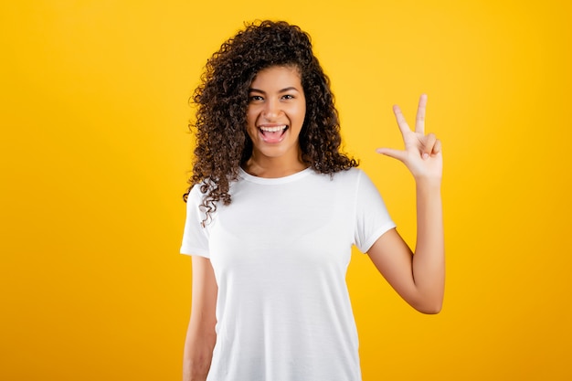 Feliz chica negra mostrando tres dedos aislados sobre amarillo