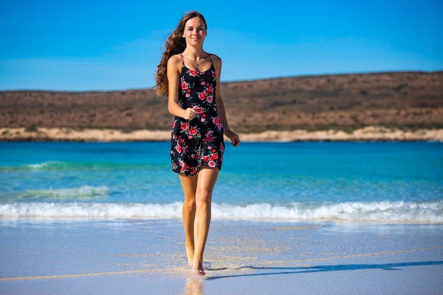 feliz chica de pelo largo con un vestido negro empapa sus piernas en agua en una bahía turquesa en el oeste de australia