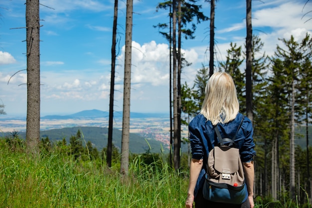 Feliz chica rubia con packpack en una montaña.