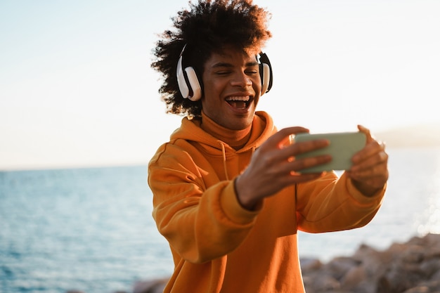 Feliz chico milenario africano escuchando lista de reproducción de música con aplicación de teléfono inteligente al aire libre