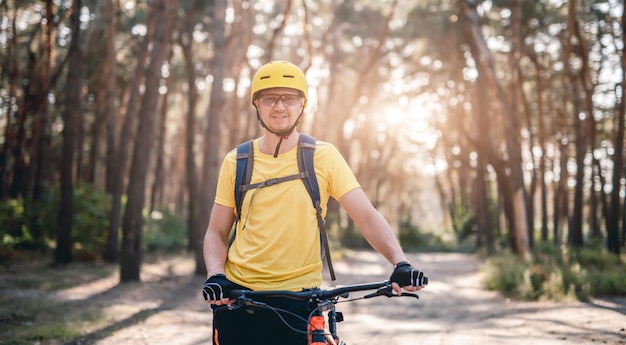 Feliz ciclista em pé com bicicleta na floresta de pinheiros