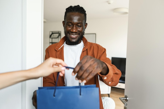 Feliz cliente afroamericano recibiendo una colorida bolsa de compras mujer entregando su pedido