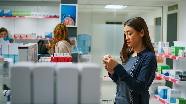 Foto feliz cliente asiático verificando pacotes de medicamentos nas prateleiras, procurando produtos de saúde para comprar na farmácia. mulher lendo caixa de comprimidos de cardiologia na farmácia, loja médica.