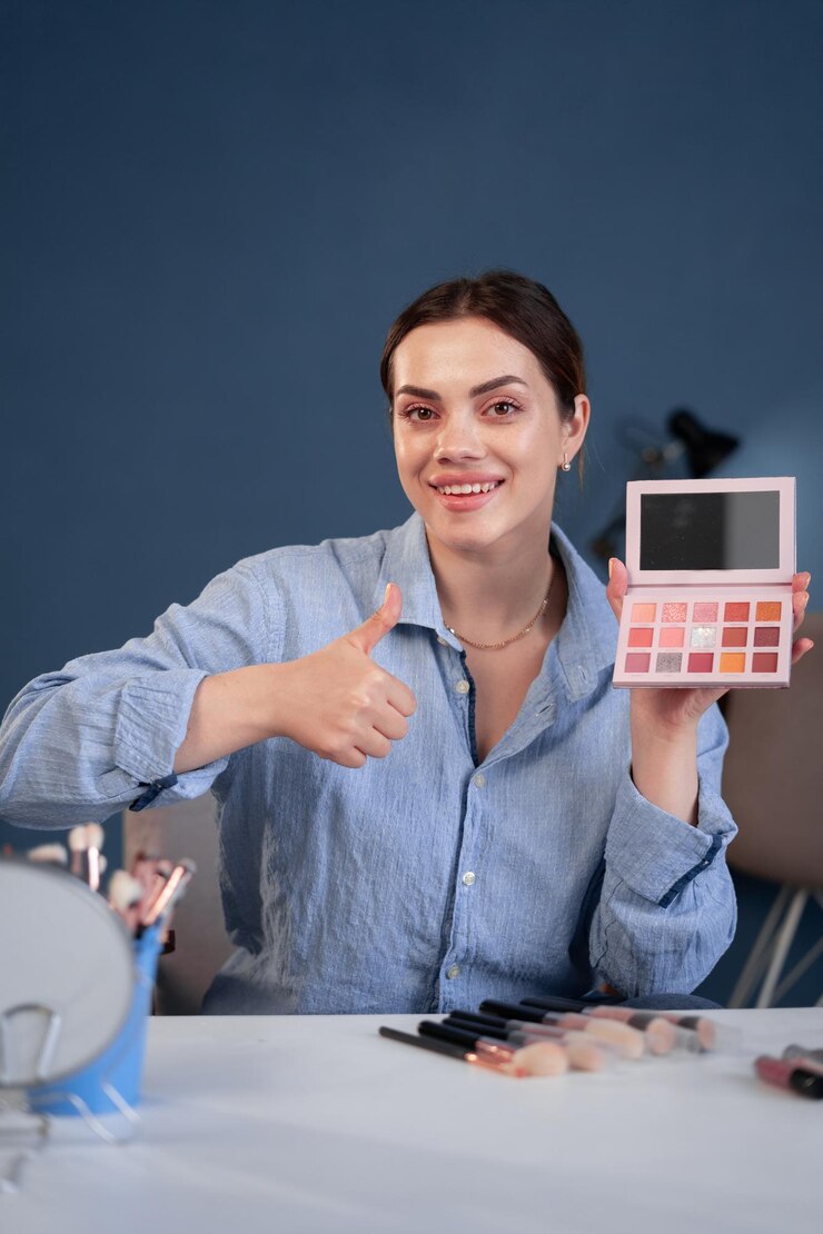 Foto feliz cliente joven caucásica blogger de belleza que muestra los pulgares hacia arriba recomienda cosméticos dispara video blog en la cámara blogger da recomendación escribe tutorial de maquillaje