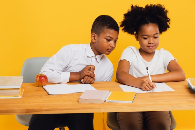 Feliz colegiala afroamericana y colegial de raza mixta sentados juntos en el escritorio y estudiando sobre fondo amarillo Concepto de regreso a la escuela