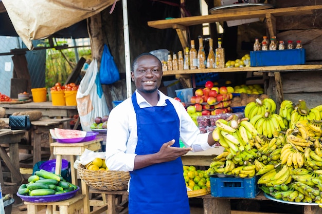 Feliz comerciante africano de frutas sonriendo sosteniendo un plátano con un colorido fondo de frutas