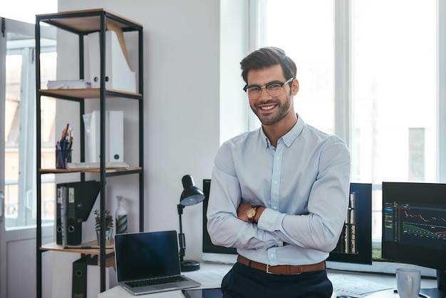 Feliz comerciante alegre empresario en ropa formal y anteojos mantiene los brazos cruzados sonriendo