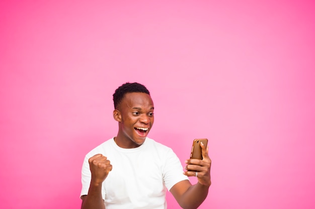 Feliz como vencedor, jovem negro animado usando telefone inteligente isolado sobre fundo rosa