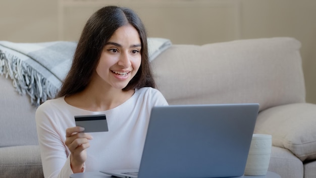 Feliz compradora árabe consumidora segura cartão bancário de plástico e digita números para aplicativo de banco on-line