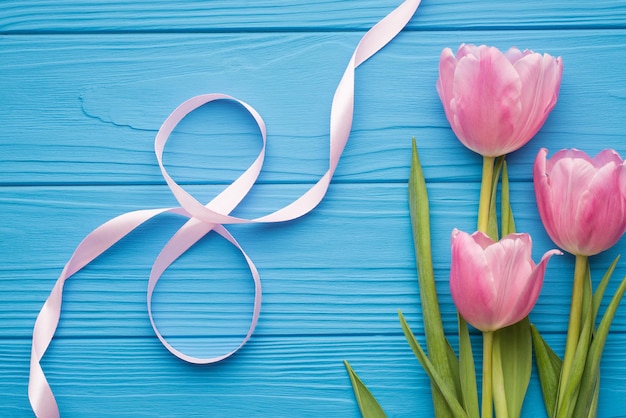 Feliz concepto del día internacional de la mujer. Arriba arriba foto de vista aérea de tres tulipanes pastel con cinta en forma de número ocho sobre fondo azul