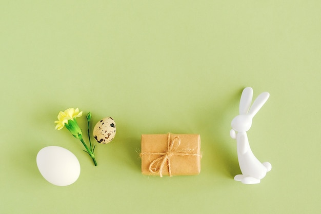 Feliz concepto de pascua. Varios huevos, flores, regalo artesanal y estatuilla de conejito sobre fondo verde con espacio de copia