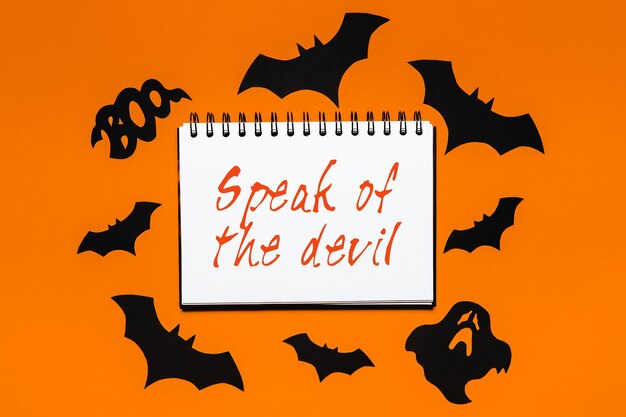 Feliz concepto de vacaciones de halloween. Bloc de notas con texto Habla del diablo sobre fondo blanco y naranja con murciélagos, calabazas y fantasmas