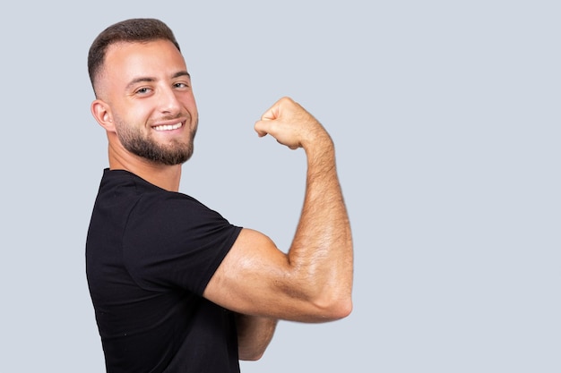 Foto feliz confiado fuerte millennial hombre caucásico entrenador en ropa deportiva mostrar músculo bíceps en la mano