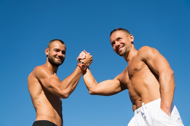 Feliz y confiado. Los hombres musculosos hacen deporte de lucha libre de brazos. Los hombres felices disfrutan de buena salud. Cuidado de la salud. Éxito en el deporte. Desarrollar fuerza y potencia muscular. La clave del éxito es la acción.