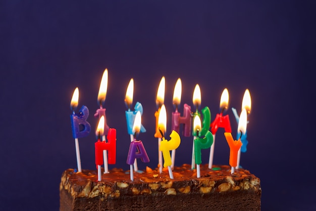 Feliz cumpleaños Brownie Cake con maní, caramelo salado y coloridas velas encendidas en la superficie violeta. Copiar espacio para texto.