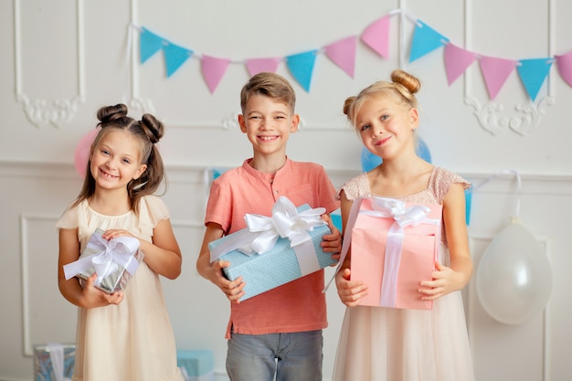 Feliz cumpleaños Felices los niños lindos en decoración festiva y hermosos vestidos con regalos en sus manos.