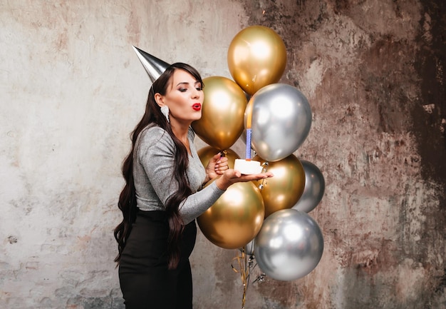 Feliz cumpleaños Morena sexy posando con globos pastel de cumpleaños de fuegos artificiales en el fondo de una pared decorativa una mujer sopla las velas en el pastel